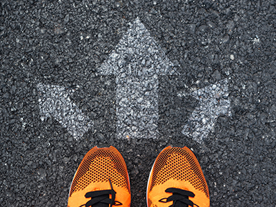 Image of yellow shoes standing on pavement with white arrows pointing in three diferent directions.